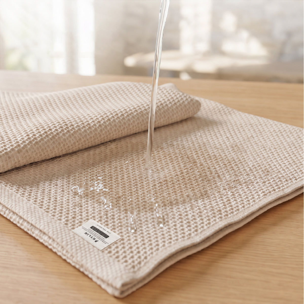 Clear water pouring onto the folded Kylin Wellness honeycomb towel, demonstrating its rapid absorbency and breathable pure cotton texture.
