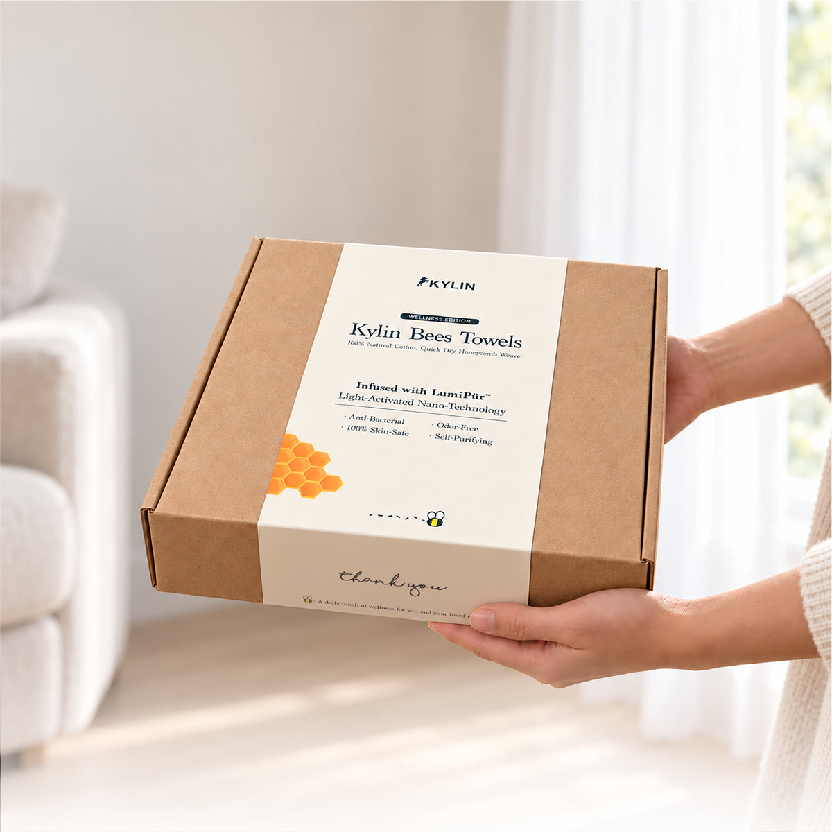 Person holding the premium packaging of the Kylin Wellness Bees Towel, showcasing the LumiPur light-activated nano-technology for a perfect skin-safe gift.